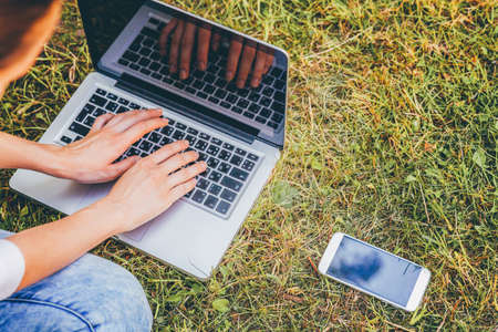 Freelance business concept. Young woman sitting on green grass lawn in city park working on laptop pc computer. Lifestyle authentic candid student girl studying outdoors. Mobile Officeの写真素材