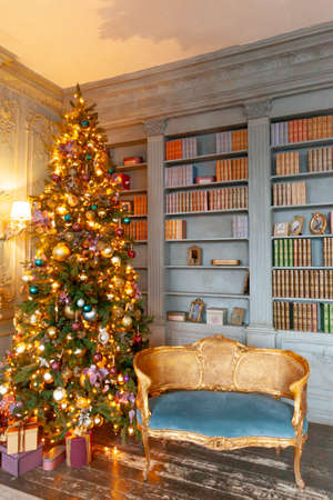 Classic Christmas New Year decorated interior room home library with fireplace. Christmas tree with gold ornament decorations. Modern classical style interior design apartment. Christmas eve at homeの写真素材