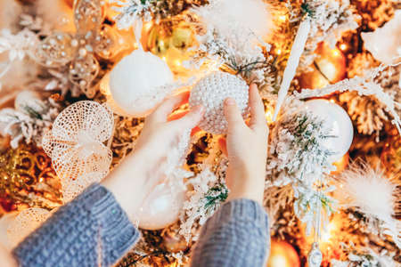 Close up girl hands decorating Christmas tree on Christmas eve at home. Young kid in light bedroom with winter decoration. Christmas New Year december time for celebration conceptの写真素材