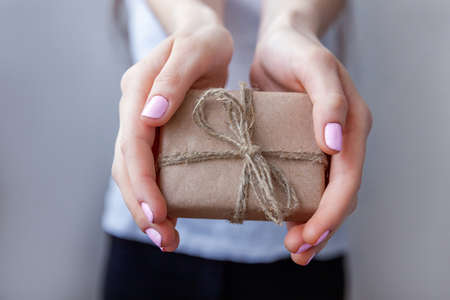 Female hands holding small gift box wrapped craft paper with ribbon. Small christmas or new year decorated gift in the hands of woman. Christmas birthday valentine celebration present romantic conceptの写真素材
