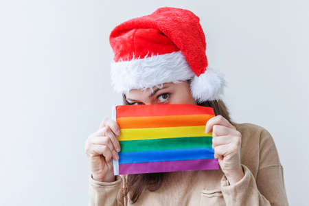 Young woman girl in red Santa Claus hat with LGBT rainbow flag isolated on white background. Happy Christmas and New Year holidays conceptの写真素材