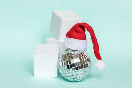 Simply minimal composition disco ball in Santa hat and cube shapes geometric form podium isolated blue pastel background. Christmas New Year december time for celebration concept. Mockup copy spaceの写真素材