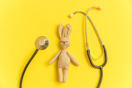Simply minimal design toy bunny and medicine equipment stethoscope isolated on yellow background. Health care children doctor concept. Pediatrician symbol. Flat lay top view layout copy spaceの写真素材