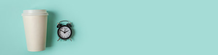 Simply minimal design paper coffee cup and alarm clock on blue pastel background. Takeaway drink and breakfast beverage. Good morning wake up awake concept. Flat lay top view copy space bannerの写真素材
