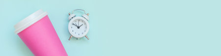 Simply flat lay design pink paper coffee cup and alarm clock isolated on blue pastel background. Takeaway drink breakfast beverage. Good morning wake up awake concept. Top view copy space bannerの写真素材