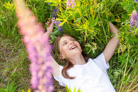 Happy teenage girl smiling outdoor. Beautiful young teen woman resting lying on summer field with blooming wild flowers green background. Free happy kid relaxing and enjoying natureの写真素材