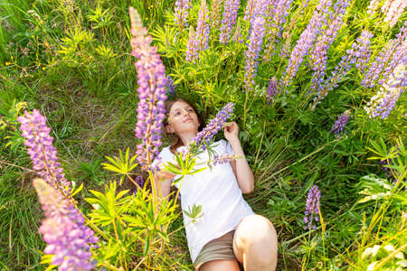 Happy teenage girl smiling outdoor. Beautiful young teen woman resting lying on summer field with blooming wild flowers green background. Free happy kid relaxing and enjoying natureの写真素材