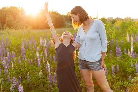 Young mother embracing her child outdoor. Woman and teenage girl on summer field with blooming wild flowers green background. Happy family mom and daughter playing on meadowの写真素材