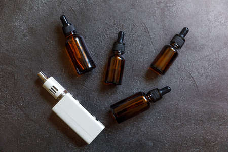 Vaping device e-cigarette electronic cigarette and liquid bottles on dark black stone shale...