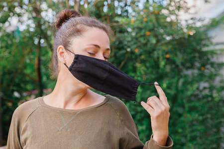 Happy positive girl takes off protective medical mask from face outdoors. Young woman removing mask smiling after vaccination.  Spring flowers pollen allergy.の写真素材