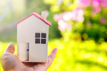 Miniature model house in female woman hand on green outdoor background. Eco Village, abstract...