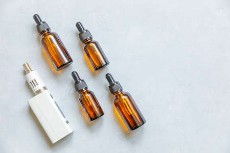 Vaping device e-cigarette electronic cigarette and liquid bottles on concrete stone gray background. Vape device for alternative smoking. Vaping shop concept. Gadget for vaper. Vaping accessoriesの写真素材