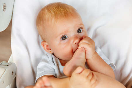 Cute little newborn girl with funny face sucking foot toe on white background. Infant baby resting...