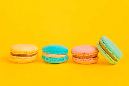 Sweet almond colorful unicorn pink blue yellow green macaron or macaroon dessert cake isolated on trendy yellow modern fashion background. French sweet cookie. Minimal food bakery concept. Copy spaceの写真素材