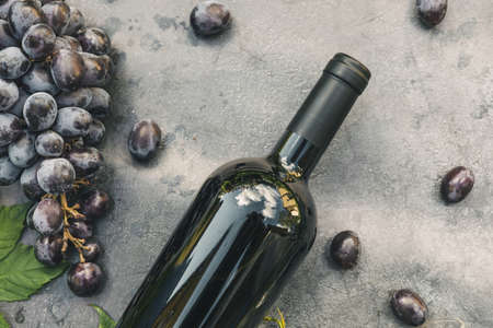 Bottle of red wine and ripe grape on vintage dark stone table background. Top view copy space for...