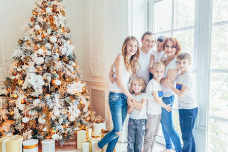 Happy family mother father five children relax playing near Christmas tree on Christmas eve at home....