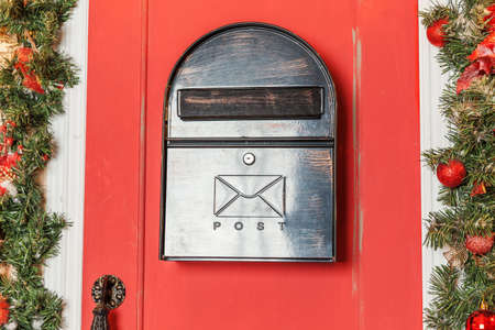 Christmas porch decoration idea. House entrance with red door decorated for holidays. Red and green wreath garland of fir tree branches and lights on railing. Christmas eve at home.の写真素材