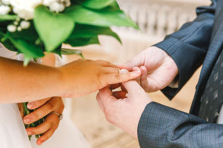 Bride and groom marriage hands with wedding rings. Groom hand putting wedding ring on bride finger. Declaration of love, spring. Wedding card greeting. Wedding day moments ceremony detailsの写真素材