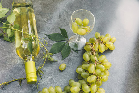 Top view of bottle white wine, green vine, wineglass and ripe grape on vintage gray stone table background. Wine shop wine bar winery or wine tasting concept.の写真素材