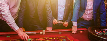 Group of people behind roulette gambling table in luxury casino. Friends playing poker at roulette table with tape measure. Vegas games nightlife lucky winning concept. Bannerの写真素材