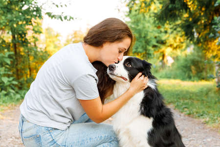 Young attractive woman playing with cute puppy dog border collie on summer outdoor background. Girl kissing holding embracing hugging dog friend. Pet care and animals conceptの写真素材
