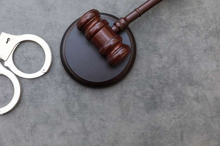 Law theme. Court of law trial in session. Judge gavel handcuffs on grey table in lawyer office or court session. Mallet of judge on concrete stone grey background. Justice human rights conceptの写真素材