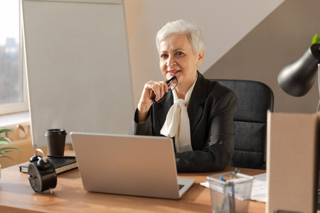 Confident stylish european middle aged senior woman using laptop at workplace. Stylish older mature 60s gray haired lady businesswoman sitting at office table. Boss leader teacher professional workerの写真素材