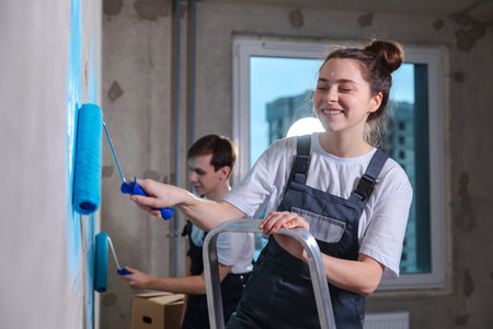 Couple in new home during repair works painting wall together. Happy family holding paint roller painting wall with blue color paint in new house. Home renovation DIY renew home conceptの写真素材