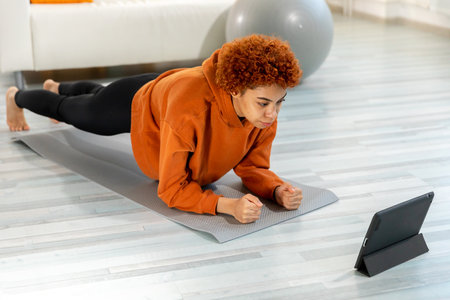 Fitness Workout training. Young healthy fit african girl doing plank exercise on yoga mat on floor...