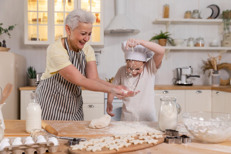 Happy family in kitchen. Grandmother and granddaughter child cook in kitchen together. Grandma teaching kid girl knead dough bake cookies. Household teamwork helping family generations conceptの写真素材