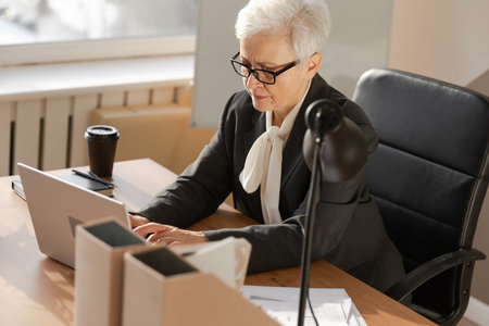 Confident stylish european middle aged senior woman using laptop at workplace. Stylish older mature 60s gray haired lady businesswoman sitting at office table. Boss leader teacher professional workerの写真素材