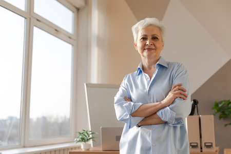 Portrait of confident stylish european middle aged senior woman at workplace. Stylish older mature 60s gray haired lady businesswoman in modern office. Boss leader teacher professional workerの写真素材
