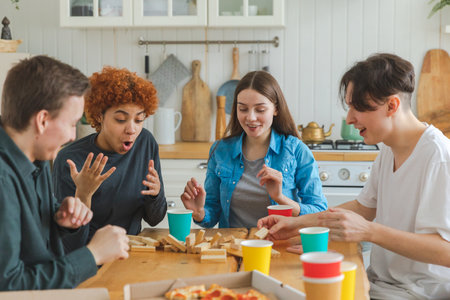 Home party. Friends spending time together playing in board game crash wooden tower at home. Happy diverse group having fun together indoor. Mixed race young buddies best friends enjoying weekendの写真素材