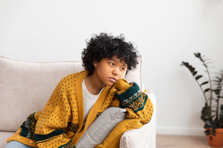 African american sad thoughtful pensive unmotivated girl sitting on sofa at home indoor. Young...