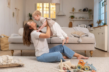 Happy family at home. Mother lifting in air little toddler child son. Mom and baby boy playing having fun together at home. Mother hugs baby with love care. Young mother kid son rest in living roomの写真素材