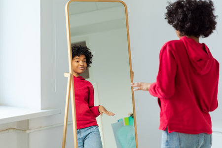Love yourself. Beautiful young smiling african american woman dancing enjoying her mirror reflection. Black lady looking at mirror looking confident and happy. Self love conceptの写真素材