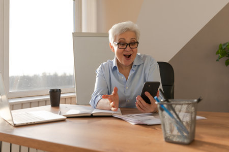Confident middle aged senior woman euphoric winner with smartphone. Older mature lady looking at cell phone reading great news getting good result winning online bid feeling amazed. Winning gestureの写真素材
