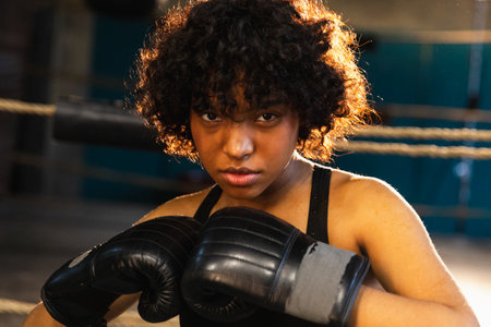 Outcry independent girl power. Angry african american woman fighter with boxing gloves looking serious aggressive standing on boxing ring. Strong powerful fighter girl training punchesの写真素材