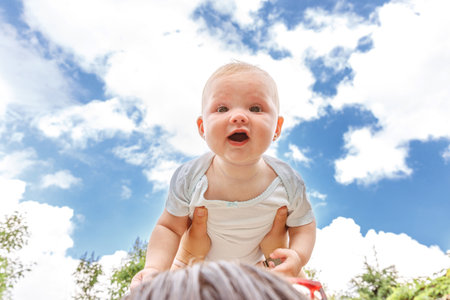 Happy family outdoor. Mother hands lifting in air little toddler baby. Mom holding embracing her child outdoor. Woman and little baby girl resting walking in park. Mother playing with babyの写真素材