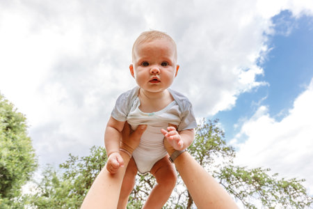 Happy family outdoor. Mother hands lifting in air little toddler baby. Mom holding embracing her child outdoor. Woman and little baby girl resting walking in park. Mother playing with babyの写真素材