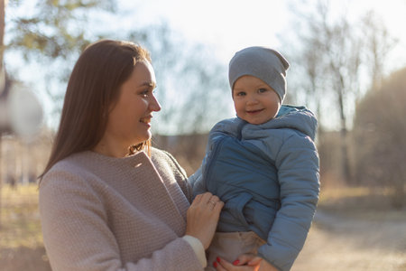 Happy family outdoor. Mother embracing her child outdoor. Mom lifting in air little toddler child son. Woman and little baby boy resting walking in park. Mother hugs baby with love careの写真素材