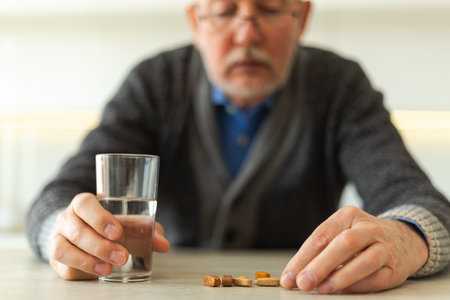 Middle aged senior man holding medical pill and glass of water. Mature old senior grandfather taking medication cure pills vitamin. Age prescription medicine healthcare therapy conceptの写真素材