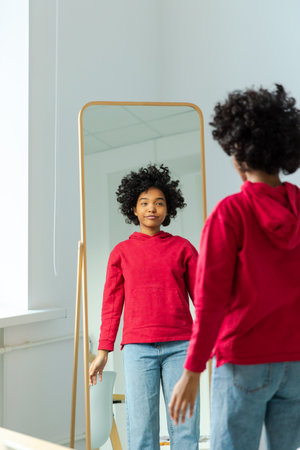 Love yourself. Beautiful young smiling african american woman dancing enjoying her mirror reflection. Black lady looking at mirror looking confident and happy. Self love conceptの写真素材