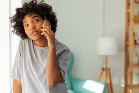 African american girl talking on smartphone at home indoor. Young woman with cell phone chatting with friends. Smiling teen girl making answering call by cellphone. Lady having conversation by mobileの写真素材