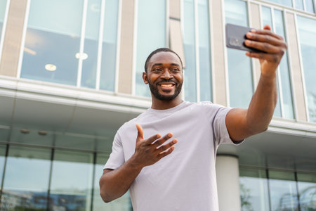 African American man holding smartphone having video chat on urban street in city. Guy blogger chatting with best friends in social network. Man having virtual meeting online chat video call outdoorの写真素材