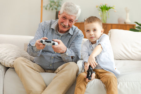 Happy family. Old senior man grandfather boy grandson playing video game with joysticks at home....