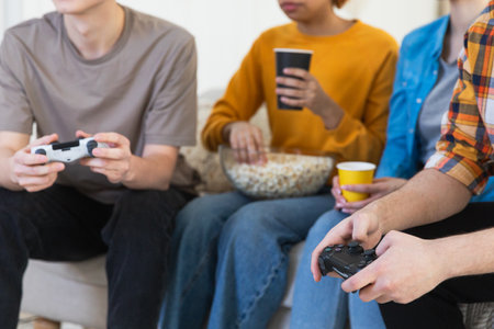 Home party. Group of friends playing video games at home, hands close up. Diverse group buddies...