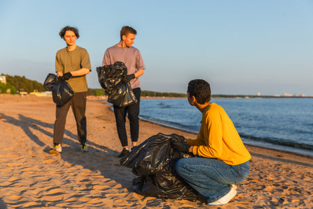 Earth day. Volunteers activists team collects garbage cleaning of beach coastal zone. Woman mans puts plastic trash in garbage bag on ocean shore. Environmental conservation coastal zone cleaningの写真素材