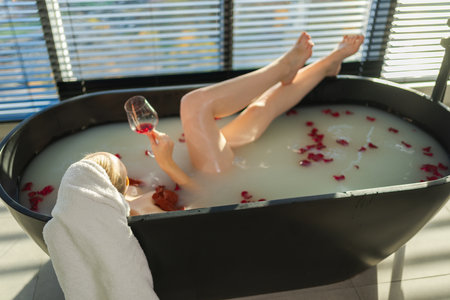 Spa relaxation. Woman lying in bath with holding glass with red wine. Girl relaxing in bathroom at home. Pretty female taking hot bath drinking wine. Stress relief. Rest after hard working dayの写真素材