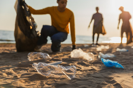 Earth day. Volunteers activists collects garbage cleaning of beach coastal zone. Woman mans with trash in garbage bag on ocean shore. Environmental conservation coastal zone cleaning. Blurred imageの写真素材